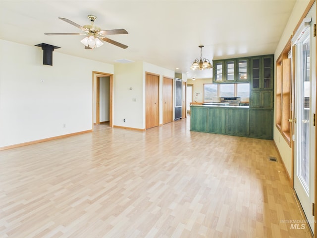 interior space with baseboards, ceiling fan with notable chandelier, light wood-style flooring, and visible vents