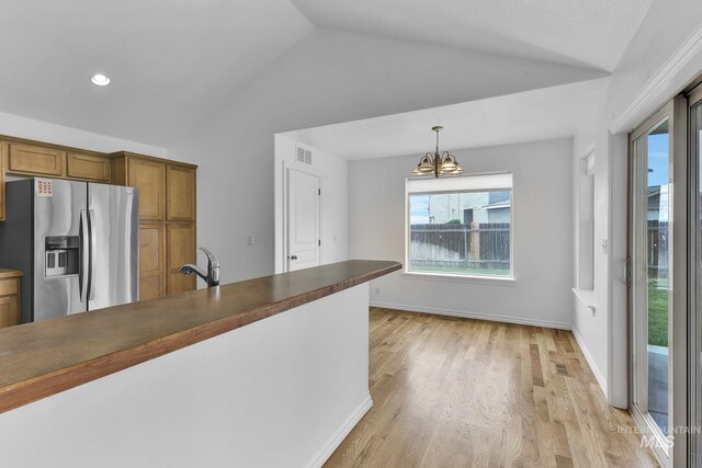 1295 NE Blossom, Mountain Home, ID 83647 - kitchen featuring stainless steel refrigerator with ice dispenser, vaulted ceiling, brown cabinetry, a chandelier, and light wood finished floors