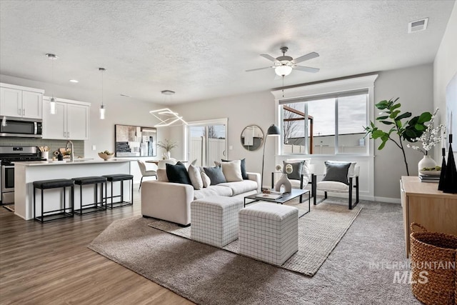 living room featuring visible vents, baseboards, dark wood-type flooring, a textured ceiling, and a ceiling fan