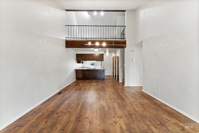 unfurnished living room featuring baseboards, a high ceiling, and dark wood-type flooring