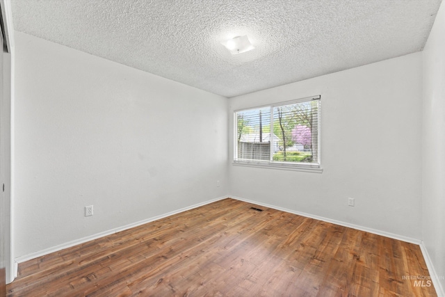 spare room featuring baseboards, a textured ceiling, wood finished floors, and visible vents