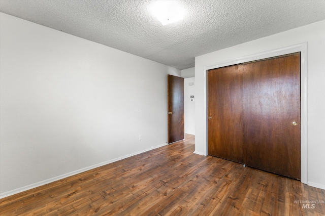unfurnished bedroom featuring a textured ceiling, dark wood-style floors, baseboards, and a closet