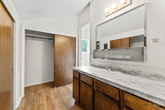 bathroom with vanity, a textured ceiling, wood finished floors, and vaulted ceiling