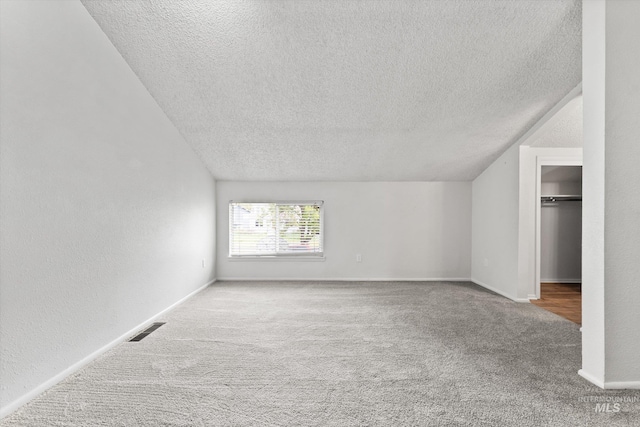 additional living space with visible vents, carpet, a textured ceiling, and vaulted ceiling
