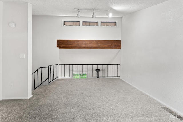 spare room featuring visible vents, a textured ceiling, carpet, and track lighting