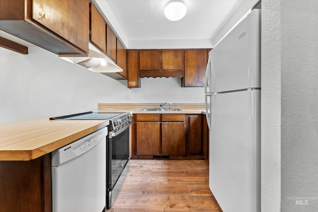 kitchen with light wood-type flooring, a sink, light countertops, under cabinet range hood, and white appliances