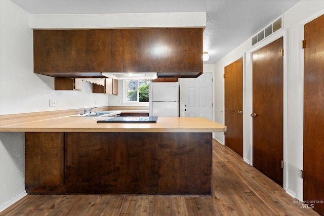 kitchen featuring visible vents, a sink, light countertops, freestanding refrigerator, and a peninsula