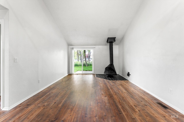 unfurnished living room with dark wood-style flooring, a wood stove, baseboards, lofted ceiling, and visible vents