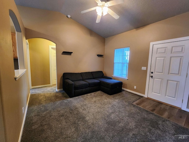 living room with a textured ceiling, ceiling fan, dark carpet, and vaulted ceiling