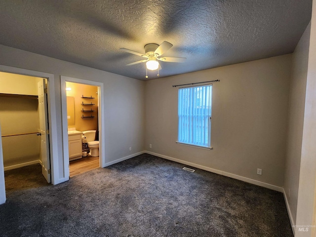 unfurnished bedroom featuring a walk in closet, dark carpet, ceiling fan, connected bathroom, and a closet