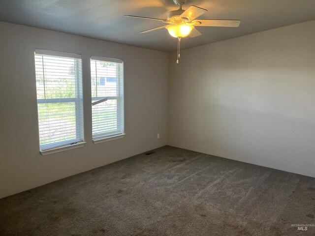 unfurnished room featuring a healthy amount of sunlight, ceiling fan, and dark carpet