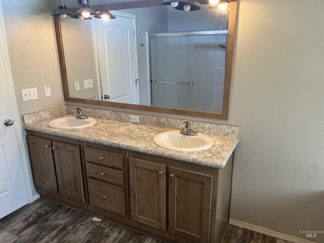 full bathroom with double vanity, a stall shower, a sink, and wood finished floors