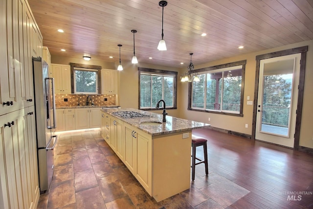 kitchen featuring dark hardwood / wood-style flooring, light stone countertops, pendant lighting, an island with sink, and wooden ceiling