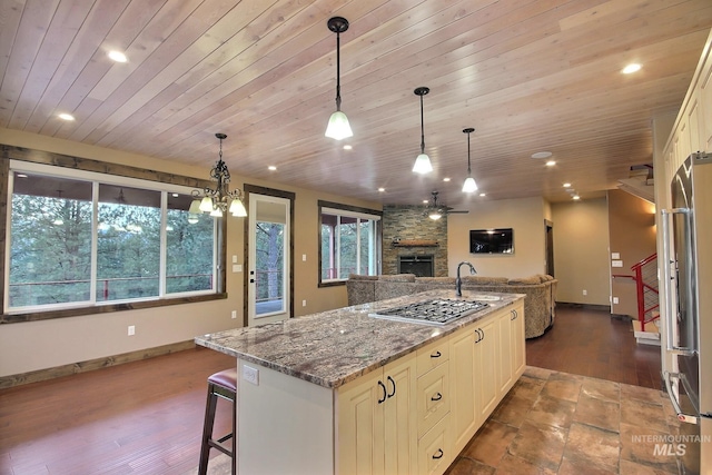 kitchen with dark stone counters, a kitchen island, a stone fireplace, appliances with stainless steel finishes, and pendant lighting