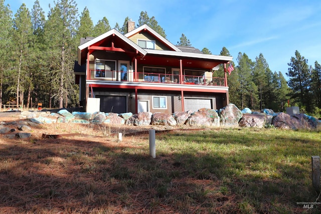 rear view of property with a garage, a lawn, and a balcony