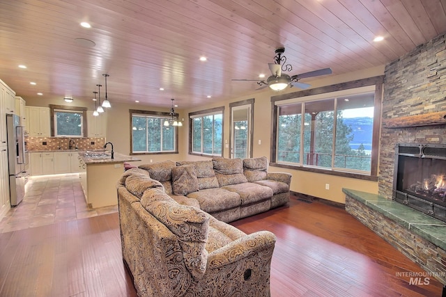 living room featuring wooden ceiling, light hardwood / wood-style floors, a stone fireplace, and ceiling fan