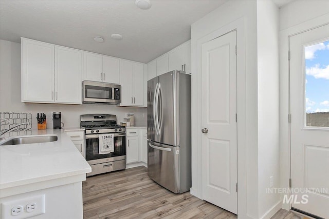 kitchen with appliances with stainless steel finishes, a sink, light wood-style floors, white cabinets, and light countertops