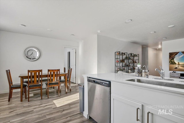 kitchen featuring dishwasher, a sink, light wood-style floors, white cabinetry, and light countertops