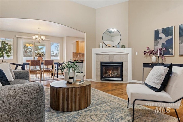 living area featuring baseboards, arched walkways, a tile fireplace, wood finished floors, and an inviting chandelier