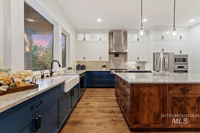 421 E Fishing Creek Ln, Eagle, ID 83616 - kitchen featuring appliances with stainless steel finishes, wall chimney range hood, a sink, blue cabinets, and light wood-type flooring