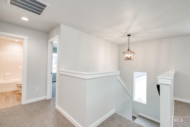 hallway with carpet flooring, an upstairs landing, visible vents, and baseboards