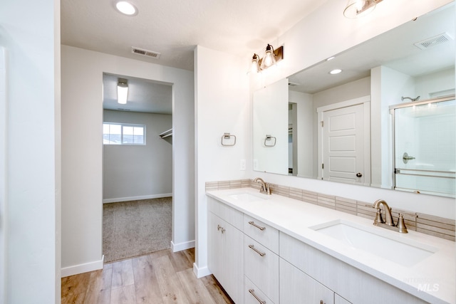 bathroom with a sink, visible vents, a shower with shower door, and wood finished floors