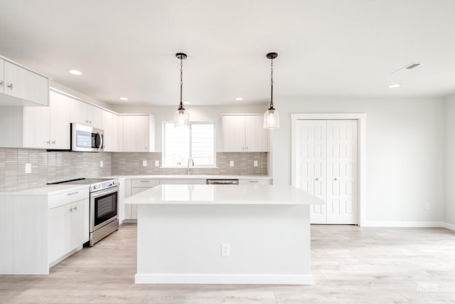 kitchen featuring tasteful backsplash, a center island, light countertops, white cabinets, and stainless steel appliances