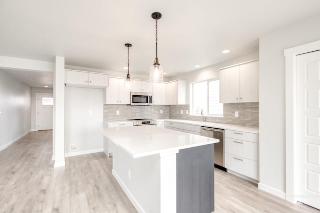 kitchen with light wood finished floors, a kitchen island, light countertops, appliances with stainless steel finishes, and white cabinets