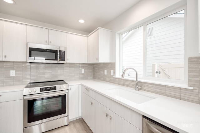 kitchen with a sink, backsplash, appliances with stainless steel finishes, and light countertops