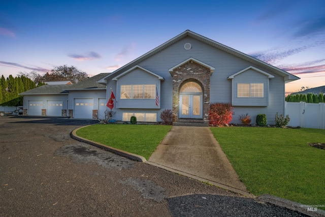 view of front of home with a front lawn, driveway, fence, french doors, and an attached garage