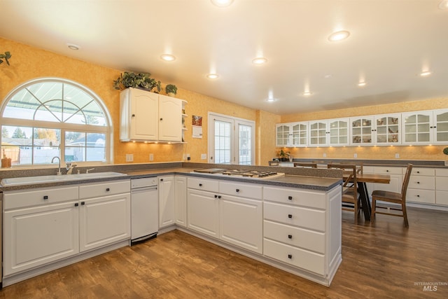 kitchen with a peninsula, dark countertops, dark wood finished floors, and a sink