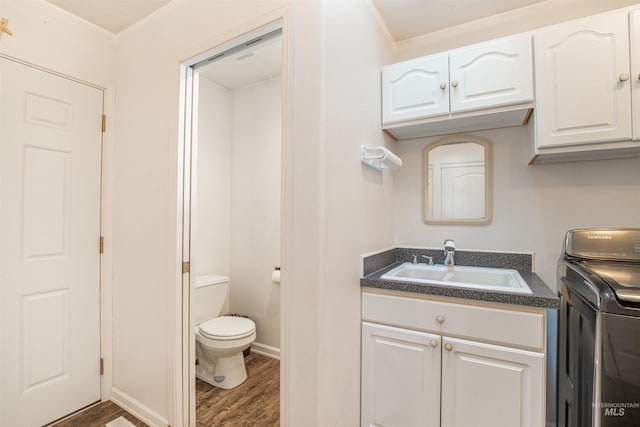 half bath with washer / dryer, baseboards, toilet, wood finished floors, and vanity