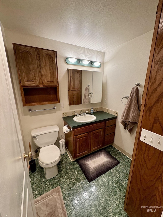 half bathroom with a textured ceiling, vanity, toilet, and baseboards