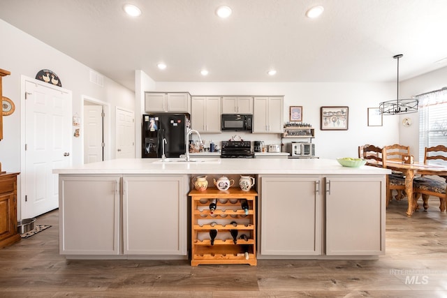 kitchen with light wood-type flooring, hanging light fixtures, a center island with sink, and black appliances