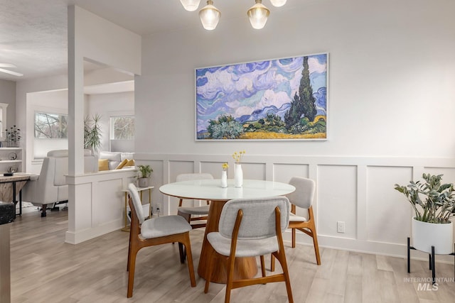 dining area with a wainscoted wall, a decorative wall, and light wood-type flooring