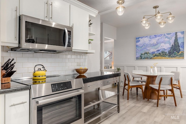 kitchen with light wood-type flooring, decorative backsplash, a decorative wall, white cabinets, and stainless steel appliances