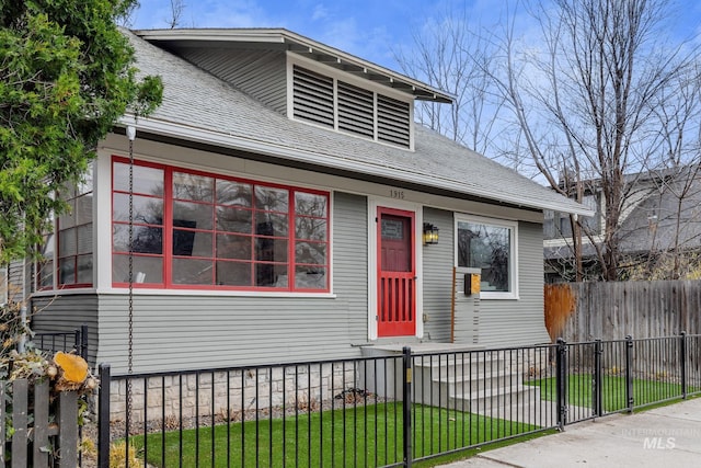 view of front of house featuring a fenced front yard, a shingled roof, and a front lawn