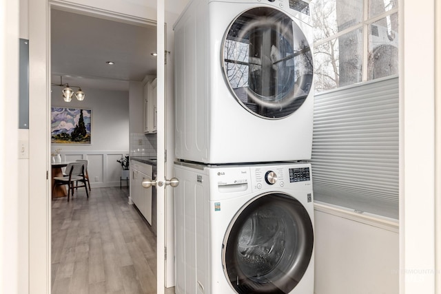 washroom with a wainscoted wall, light wood finished floors, laundry area, stacked washer and dryer, and a decorative wall