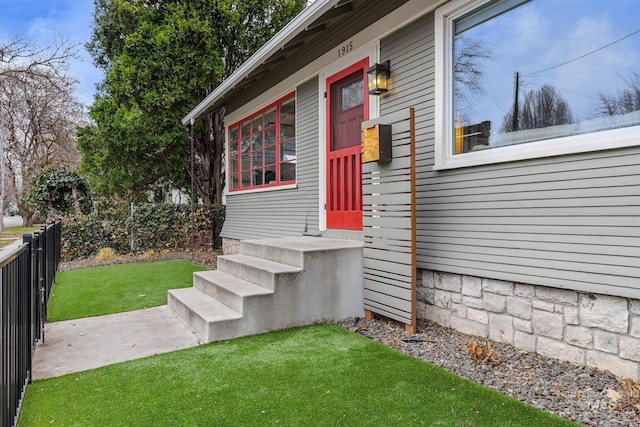 view of exterior entry featuring a lawn and fence