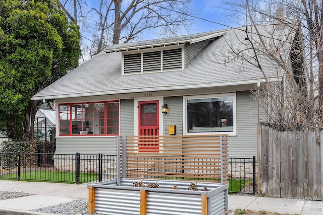 bungalow-style home featuring a fenced front yard, roof with shingles, and a vegetable garden