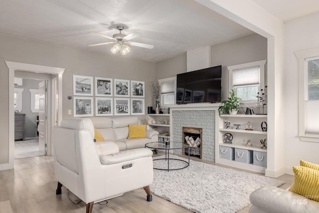 living area featuring wood finished floors, a brick fireplace, a ceiling fan, and baseboards