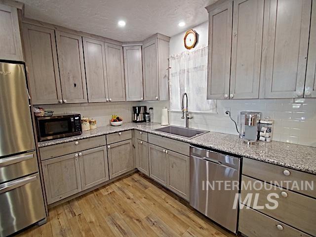 kitchen featuring sink, tasteful backsplash, appliances with stainless steel finishes, light stone countertops, and light hardwood / wood-style floors