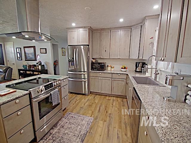 kitchen featuring sink, stainless steel appliances, light stone counters, island exhaust hood, and light wood-type flooring