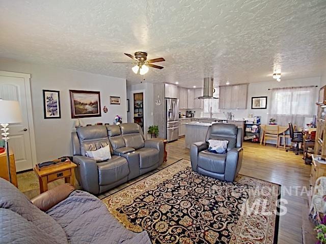 living room featuring ceiling fan, a textured ceiling, and light hardwood / wood-style floors