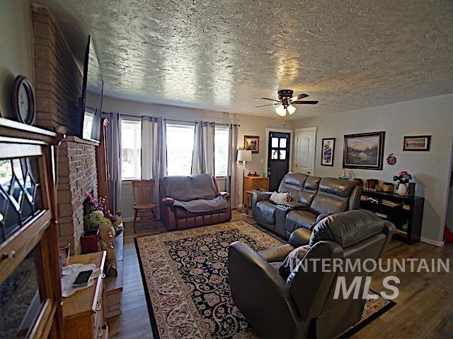 living room with a brick fireplace, hardwood / wood-style floors, a textured ceiling, and ceiling fan