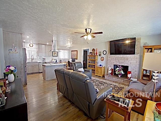 living room with sink, light hardwood / wood-style flooring, ceiling fan, a fireplace, and a textured ceiling