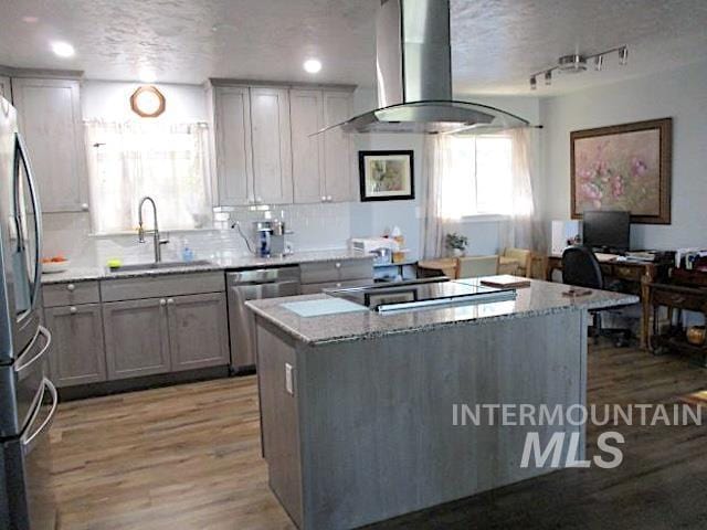 kitchen with sink, stainless steel appliances, a center island, light stone countertops, and island exhaust hood