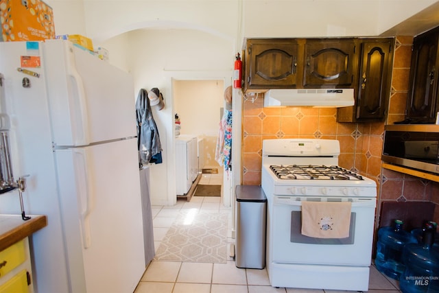 599 S Ada St, Glenns Ferry, ID 83623 - kitchen featuring under cabinet range hood, white appliances, light tile patterned floors, washing machine and clothes dryer, and arched walkways