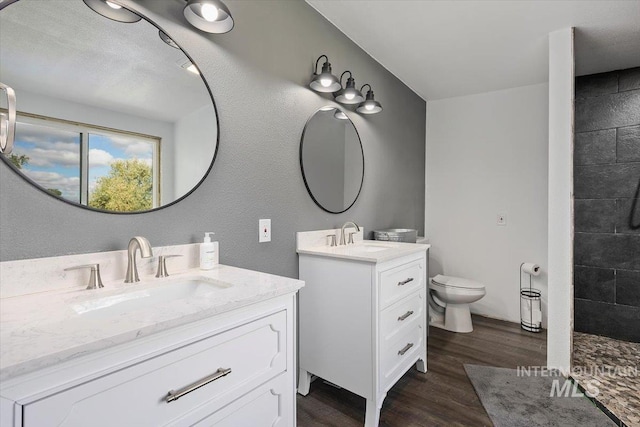 bathroom with hardwood / wood-style floors, tiled shower, vanity, and toilet