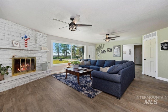 living room with a textured ceiling, a stone fireplace, dark hardwood / wood-style floors, and ceiling fan